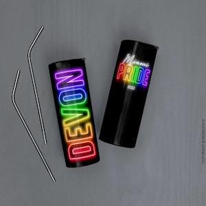 K&ouml;nnte beinhalten: Zwei schwarze Edelstahlbecher mit Regenbogen-Neon-Designs. Ein Becher sagt "DEVON" und der andere sagt "Miami Pride 2022".