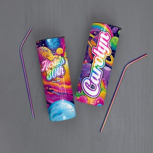 May include: Two personalized tumblers with a vibrant space-themed design, featuring planets, rainbows, and the names "Alexia's 80th" and "Carolyn". Two iridescent straws are also present. The tumblers are cylindrical and likely insulated.