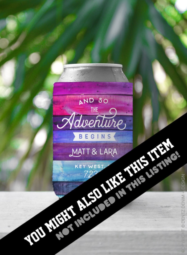 May include: A can cooler with a colorful, rustic wood-grain design. The text "AND SO THE Adventure BEGINS" is displayed, along with names and a date. The background is blurred green foliage.