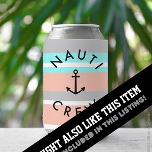 May include: A gray can cooler with the words "NAUTI CREW" and an anchor graphic. The cooler has horizontal stripes in light blue, peach, and gray. The background is blurred green foliage.