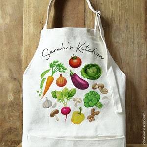 May include: White cotton apron with a pocket, featuring a colorful illustration of vegetables and the text "Sarah's Kitchen".