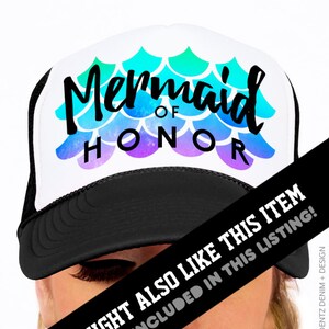 May include: A white trucker hat with a black brim and mesh back. The hat features the text "Mermaid of Honor" in black script, with a mermaid scale design in shades of blue, green, and purple.