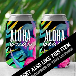 May include: Two silver can coolers with a tropical design. The coolers feature the words "ALOHA bride" and "ALOHA bea" in white script. The design includes pink, blue, and green tropical leaves and flowers against a black background.