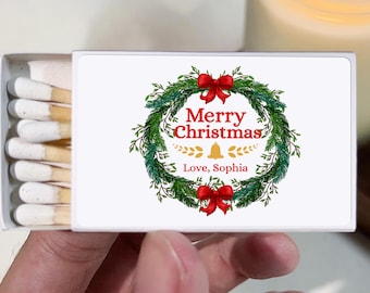 May include: A matchbox with a festive Christmas design. The box features a wreath with red bows, the words "Merry Christmas," and the name "Sophia." The matches are visible inside the open box.