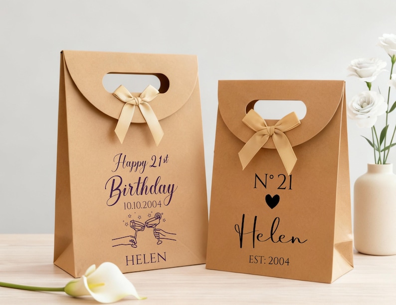 Pode incluir: Duas sacolas de presente de papel marrom com al&ccedil;as e la&ccedil;os. Uma sacola diz "Happy 21st Birthday" com uma data e um nome. A outra sacola tem "N 21" com um cora&ccedil;&atilde;o, um nome e o ano de 2004.