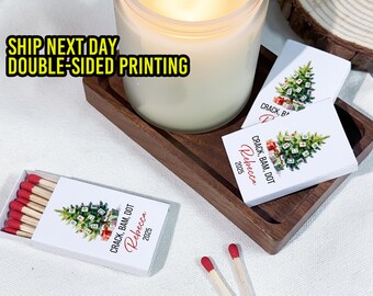 May include: A lit candle sits on a wooden tray with matchboxes and matchbooks. The matchboxes and matchbooks have a Christmas tree design with the text "CRACK, BAM, DOT Rebecca 2025". The matches have red tips.