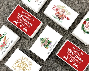 May include: A collection of personalized Christmas-themed gift boxes. The boxes feature various designs, including Santa Claus, Christmas trees, reindeer, and festive text like "Merry Christmas" and family names. The boxes are white with red, green, and gold accents.