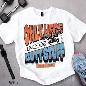 May include: White t-shirt with a graphic design featuring the text "ONLY HERE FOR BUTT STUFF" in orange and blue, along with an illustration of a weightlifter. The phrase "SHUT UP AND SQUAT" is also included.
