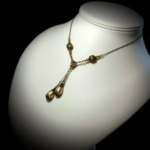 May include: A gold tone necklace with a delicate chain and multiple small round beads. The necklace has two pearlescent teardrop pendants at the end.