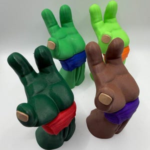 May include: Four 3D-printed hand sculptures making a peace sign gesture. Each hand features a colored wristband: one dark green with red, one medium green with blue, one light green with orange, and one brown with a purple wristband.