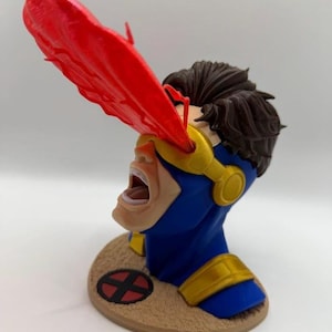 May include: A bust of the X-Men character Cyclops, featuring a blue and gold costume with a red optic blast. The figure has brown hair and is mounted on a circular base with the X-Men logo.