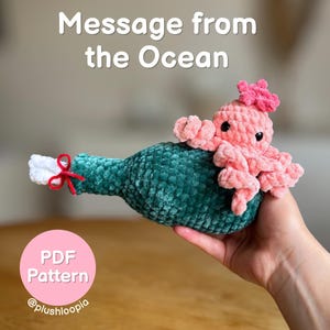 May include: A crocheted plush toy featuring a dark green bottle shape with a white paper scroll tied by a red string at the neck, topped with a small pink octopus. The text Message from the Ocean and a pink circle with PDF Pattern @plushloopia appear.
