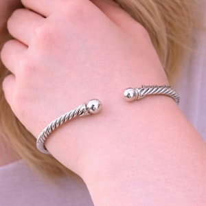 Puede incluir: Un brazalete de plata con un diseño de cuerda trenzada. El brazalete tiene un extremo en forma de bola en cada lado. El texto "VinitaSilverShop" es visible en el brazalete.
