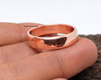 May include: A polished, rose gold ring with a smooth, rounded band. The ring is held in a hand, showcasing its reflective surface. The ring's design is simple and elegant, suitable for everyday wear. The ring is a classic piece of jewelry.