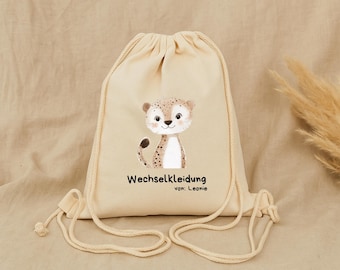 Op de afbeelding: Een beige trekkoordtas met een cartoon illustratie van een cheetah. De cheetah heeft bruine vlekken en lacht. De tekst "Wechselkleidung" en "von: Leonie" staan eronder.