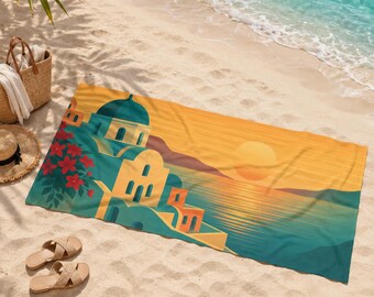 May include: A beach towel featuring a scenic illustration of a coastal village with blue-domed buildings, red flowers, and a sunset over the sea. The towel is rectangular and lies on a sandy beach, with accessories like a straw hat and sandals.