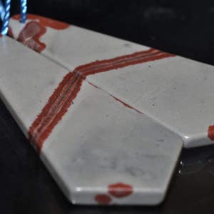 May include: A pair of gray and red stone earrings with a geometric shape. The earrings are connected by a blue string.