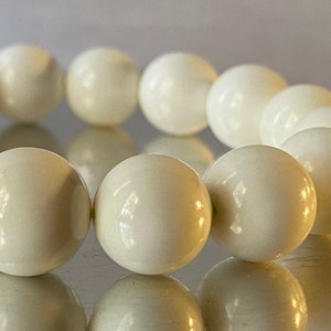 Può includere: Un braccialetto di perline bianche con perline rotonde e lisce. Il braccialetto è fatto di pietra naturale e ha una finitura lucida.