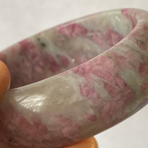 May include: A pink and white stone bangle bracelet with a smooth, polished finish. The stone has a swirling pattern of pink and white.