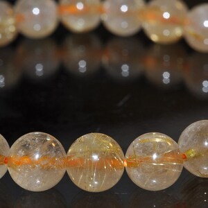 May include: A bracelet made of clear quartz beads with gold and orange inclusions. The beads are round and have a smooth, polished finish.