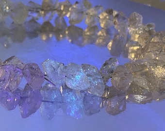 Könnte beinhalten: Eine Kette aus klaren Quarzkristallperlen mit einem leichten violetten Farbton. Die Perlen sind facettiert und haben ein raues, natürliches Aussehen. Die Perlen sind auf einem Draht aufgefädelt und in einem Kreis angeordnet.