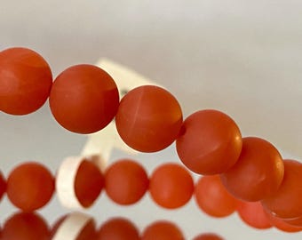 May include: A close-up of a strand of orange coral beads. The beads are round and smooth, and they are strung together on a clear string.