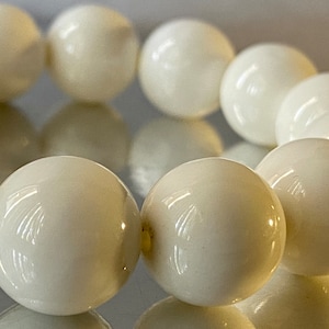 Puede incluir: Un brazalete de perlas blancas con cuentas redondas y lisas. El brazalete está hecho de perlas naturales y tiene un diseño clásico y elegante.