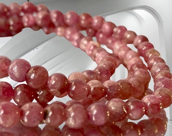May include: A close-up of a pink gemstone bracelet with multiple strands of round beads. The beads are smooth and shiny, and the bracelet is arranged in a circular shape.