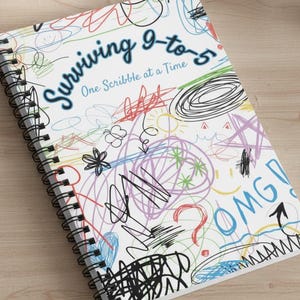 May include: A spiral-bound notebook with a white cover featuring colorful scribbles and the text "Surviving 9-to-5 One Scribble at a Time." The design includes doodles, stars, and the word "OMG!" in blue.