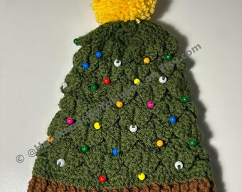 Peut inclure: Un bonnet fait à la main en forme de sapin de Noël avec un pompon jaune sur le dessus. Le bonnet vert est décoré de perles colorées pour ressembler à des lumières de Noël. Le bas du bonnet est marron.