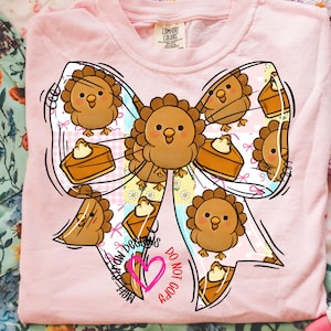 Könnte beinhalten: Hellrosa Comfort Colors Sweatshirt mit einem großen Schleifendesign mit Cartoon-Truthähnen und Kürbiskuchenstücken. Der Bogen hat ein Blumenmuster und den Text "Melt My Designs" und "Do Not Copy".