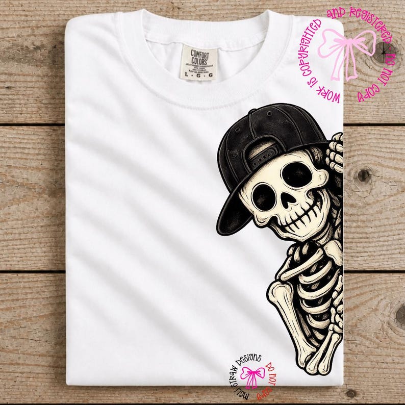Op de afbeelding: Een wit t-shirt met een grafische illustratie van een skelet dat een zwarte honkbalpet draagt. Het skelet is aan de rechterkant van het shirt geplaatst en kijkt vanaf de rand naar buiten. Het shirt heeft een Comfort Colors merklabel in de nek.