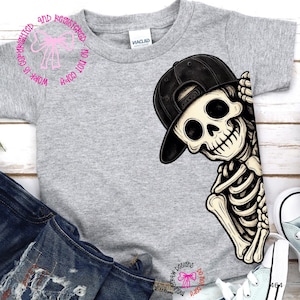 Op de afbeelding: Een grijs gem&ecirc;leerd T-shirt met korte mouwen en een grafische print van een skelet met een zwarte honkbalpet. Het skelet is aan de rechterkant van het shirt geplaatst en lijkt achter de rand vandaan te komen met een hand bij de pet.