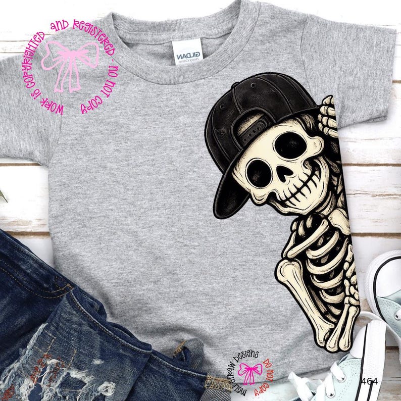 Op de afbeelding: Een grijs gem&ecirc;leerd T-shirt met korte mouwen en een grafische print van een skelet met een zwarte honkbalpet. Het skelet is aan de rechterkant van het shirt geplaatst en lijkt achter de rand vandaan te komen met een hand bij de pet.