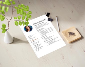 May include: A CV for Alexandra Smith, a Junior SOC Analyst, is displayed on a light wooden surface. The CV includes a photo, contact information, and details about education, skills, and experience. A white vase with green leaves, a pencil, paper clips, and a wooden dish are also present.