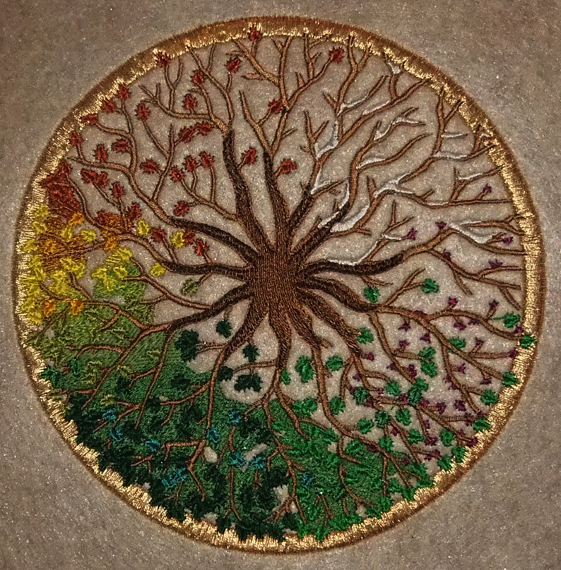 Puede incluir: Dise&ntilde;o circular bordado de un &aacute;rbol con ramas de diferentes colores que representan las cuatro estaciones. El &aacute;rbol est&aacute; rodeado por un borde dorado.