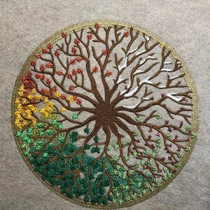 Puede incluir: Dise&ntilde;o bordado de un &aacute;rbol con ramas de diferentes colores que representan las cuatro estaciones. El &aacute;rbol est&aacute; rodeado por un c&iacute;rculo dorado.