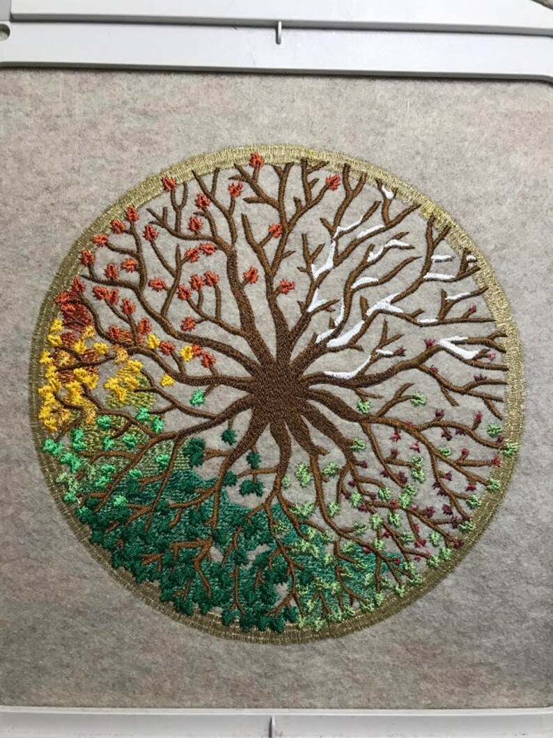 Puede incluir: Dise&ntilde;o bordado de un &aacute;rbol con ramas de diferentes colores que representan las cuatro estaciones. El &aacute;rbol est&aacute; rodeado por un c&iacute;rculo dorado.