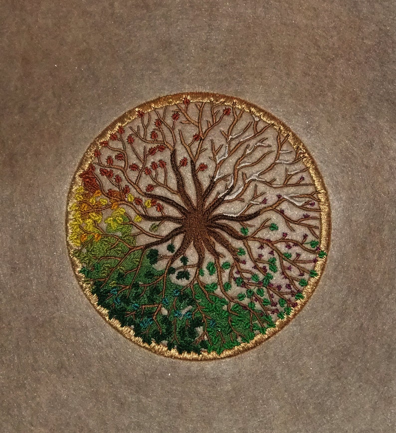 Puede incluir: Dise&ntilde;o bordado en c&iacute;rculo de un &aacute;rbol con ra&iacute;ces y ramas, que muestra las estaciones cambiantes con hojas de diferentes colores. El &aacute;rbol est&aacute; rodeado por un c&iacute;rculo dorado.