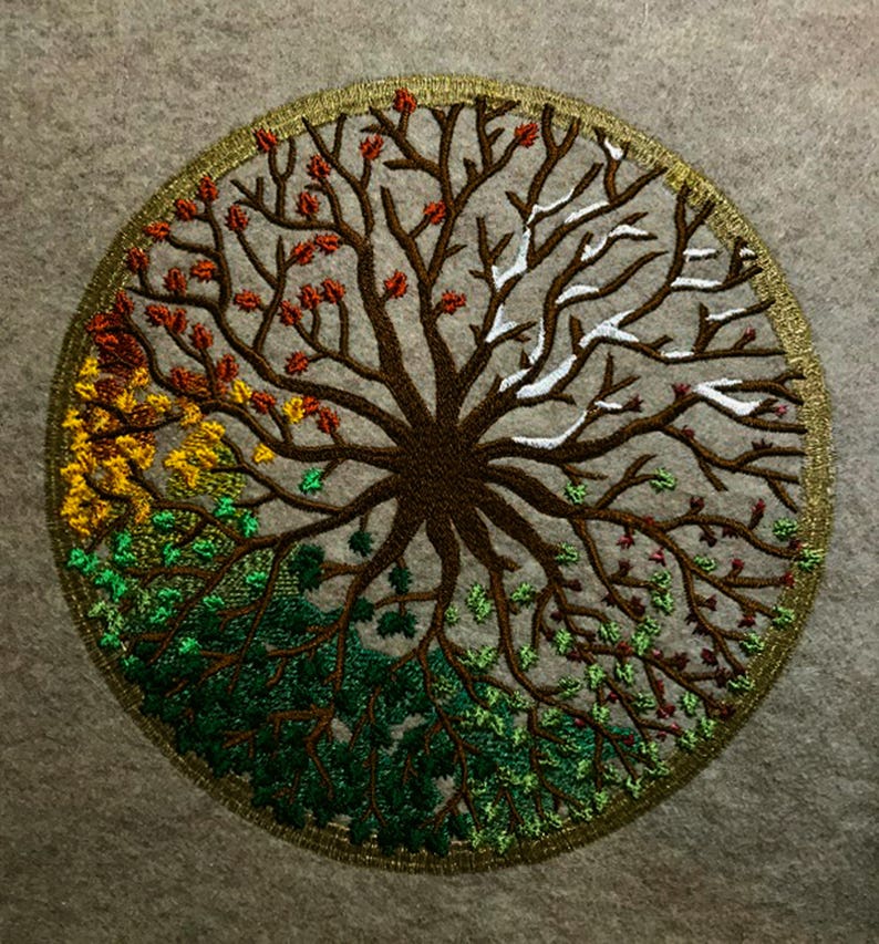 Puede incluir: Dise&ntilde;o circular bordado de un &aacute;rbol con ramas de diferentes colores que representan las cuatro estaciones. El &aacute;rbol es marr&oacute;n con hojas verdes, amarillas, rojas y blancas.