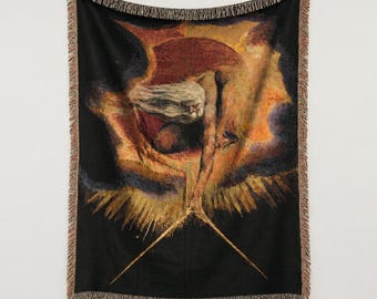 Puede incluir: Una manta tejida con una reproducción de The Ancient of Days de William Blake. El diseño muestra una figura barbuda que extiende un compás dorado hacia abajo sobre un fondo oscuro y ardiente, con bordes de flecos.