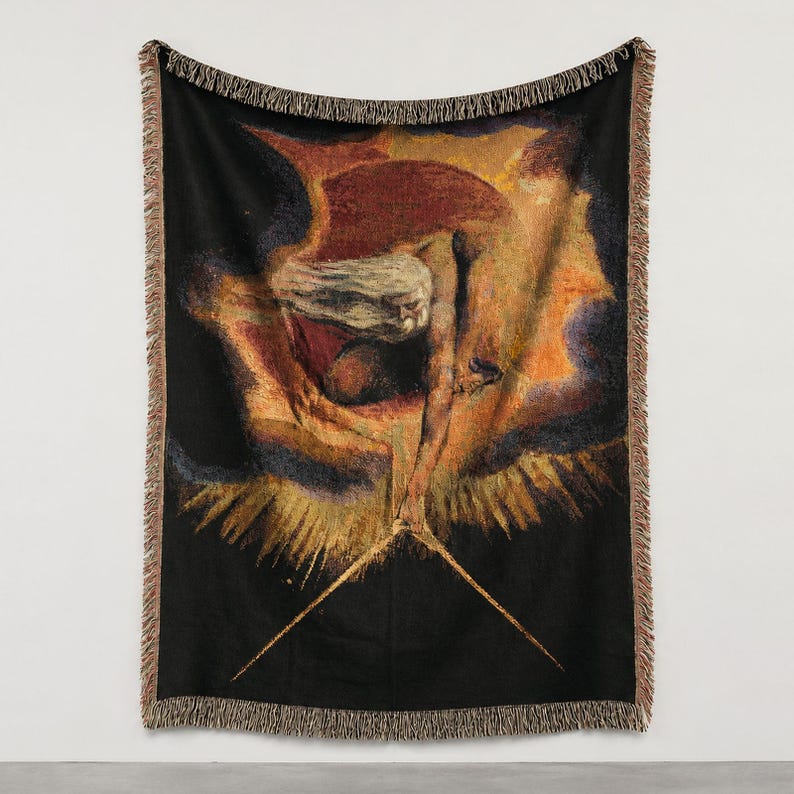Puede incluir: Una manta tejida con una reproducci&oacute;n de The Ancient of Days de William Blake. El dise&ntilde;o muestra una figura barbuda que extiende un comp&aacute;s dorado hacia abajo sobre un fondo oscuro y ardiente, con bordes de flecos.