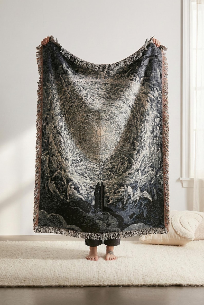 May include: A rectangular woven throw blanket featuring a detailed monochromatic illustration of a celestial scene with a central radiant light source, winged figures, and two dark silhouettes standing at the base, finished with fringed edges.