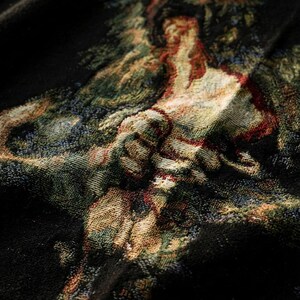 Pu&ograve; includere: Un tessuto nero caratterizzato da un design a arazzo intrecciato con una scena multicolore che raffigura una figura in un paesaggio. L'intreccio complesso incorpora fili nei toni del verde, rosso, oro e crema, creando un motivo visivo dettagliato.