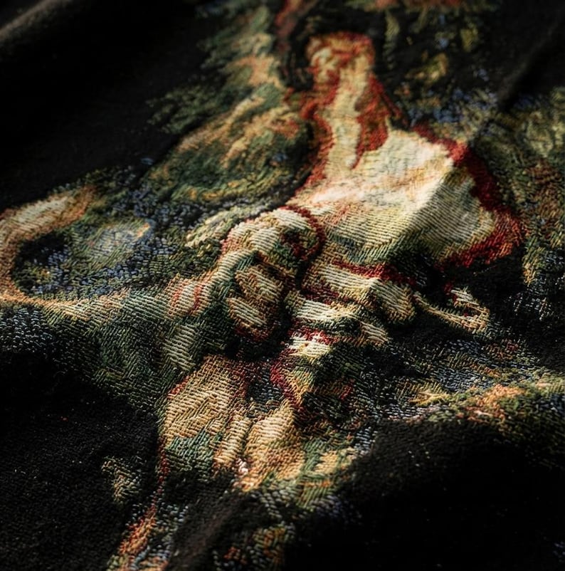 Pu&ograve; includere: Un tessuto nero caratterizzato da un design a arazzo intrecciato con una scena multicolore che raffigura una figura in un paesaggio. L'intreccio complesso incorpora fili nei toni del verde, rosso, oro e crema, creando un motivo visivo dettagliato.
