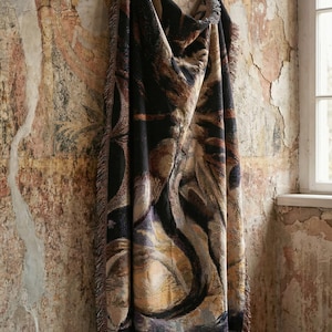 Puede incluir: Una manta tejida rectangular con un dise&ntilde;o abstracto oscuro que presenta patrones de remolinos en tonos negro, marr&oacute;n oscuro, dorado y morado apagado. La manta tiene una superficie texturizada y bordes deshilachados en los lados.