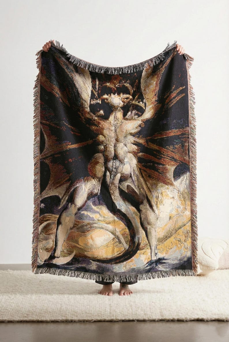 Puede incluir: Una manta tejida rectangular que presenta una ilustraci&oacute;n detallada de una criatura alada y con cuernos con una cola larga. El dise&ntilde;o utiliza un fondo negro oscuro con tonos beige, marrones y dorados. La manta tiene bordes con flecos.