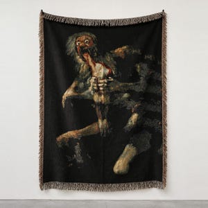 Pu&ograve; includere: Una coperta tessuta con una riproduzione di Saturno che divora suo figlio di Francisco Goya. L'arazzo scuro e strutturato mostra una figura dagli occhi sgranati che consuma una forma pi&ugrave; piccola su sfondo nero, con bordi sfrangiati.
