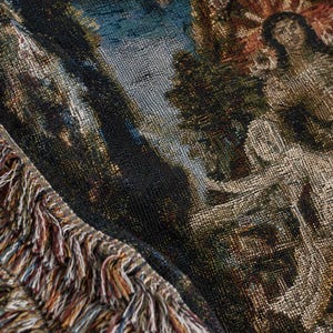 Puede incluir: Una manta de tapiz tejida que presenta una escena detallada con figuras, &aacute;rboles y elementos arquitect&oacute;nicos en tonos negro, dorado, azul y crema. La tela tiene un tejido texturizado y un borde decorativo con flecos de hilos multicolores.
