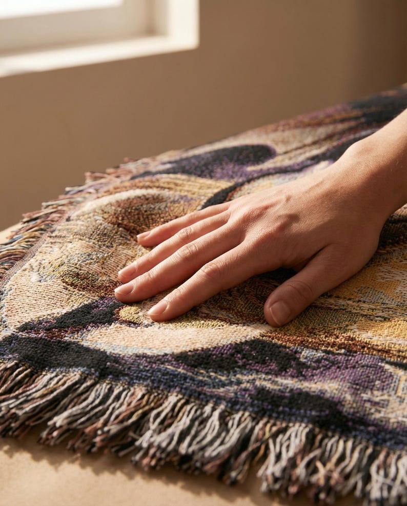 Puede incluir: Una manta tejida con un patr&oacute;n abstracto multicolor en tonos morado, negro, bronceado y dorado. El tejido tiene una textura similar a un tapiz y est&aacute; rematado con un fleco decorativo a lo largo del borde curvo.